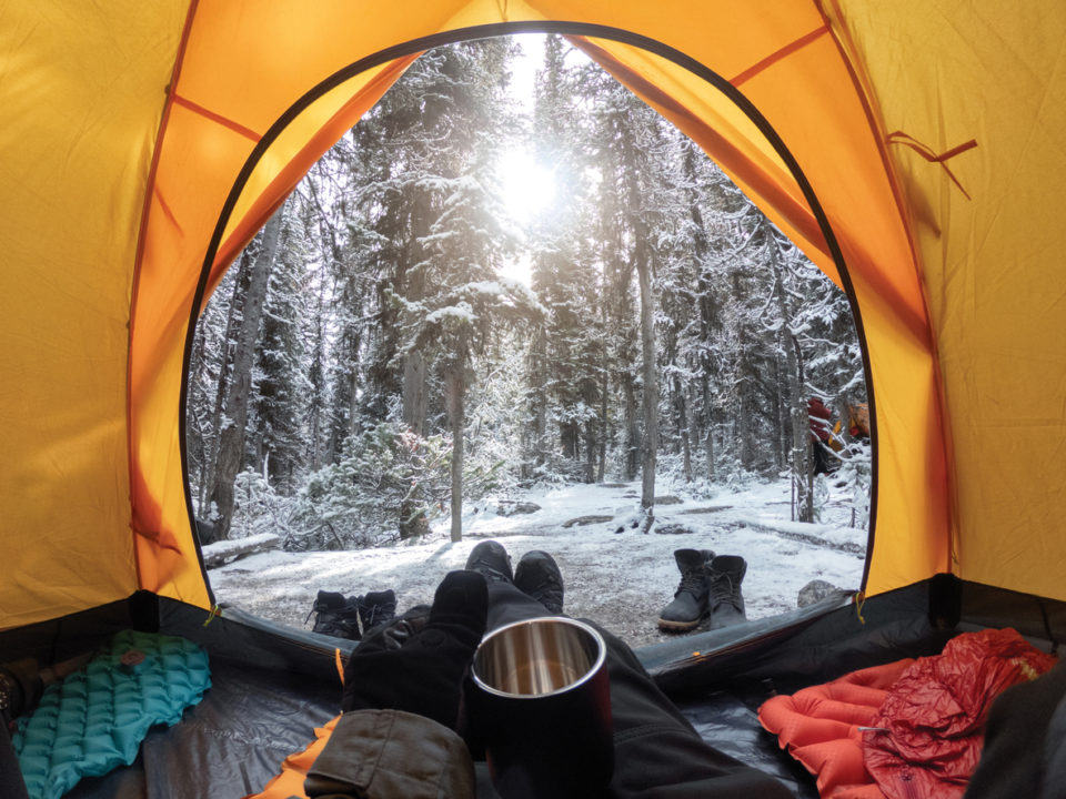 Camping with hand holding cup in yellow tent with snow in pine forest