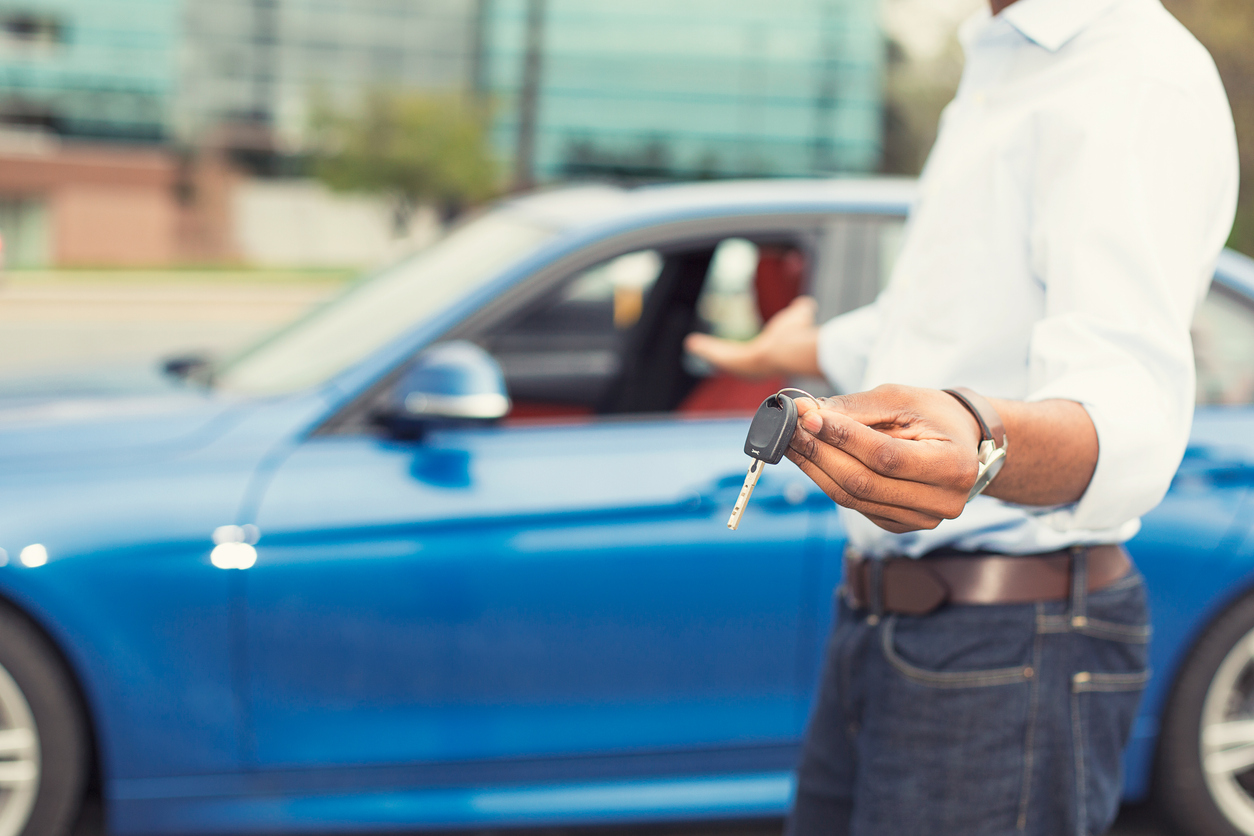 Male hand holding car keys offering car on background