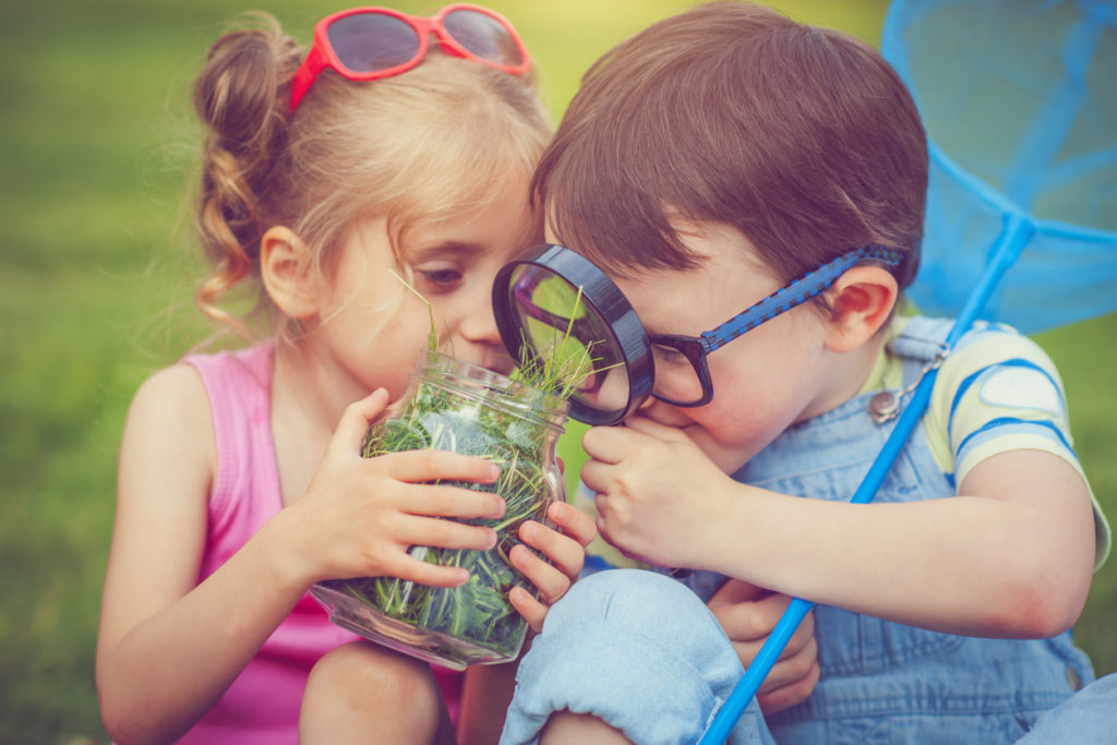 Little boy and girl exploring the world with grass and magnifying glass.