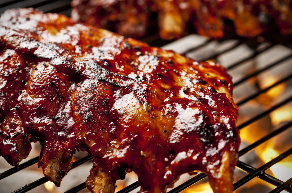 close up of pork ribs covered in bbq sauce on grill