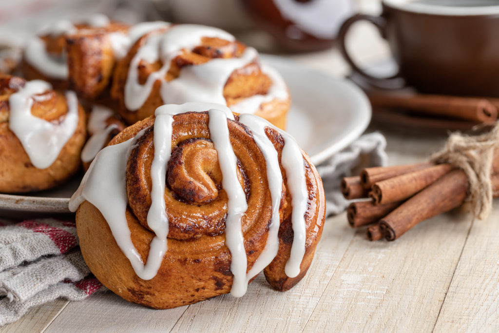 Closeup of a baked cinnamon roll with white icing on a wooden table