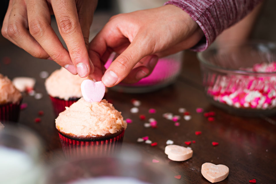 Hands of a couple decorating cupcakes for valentine's day