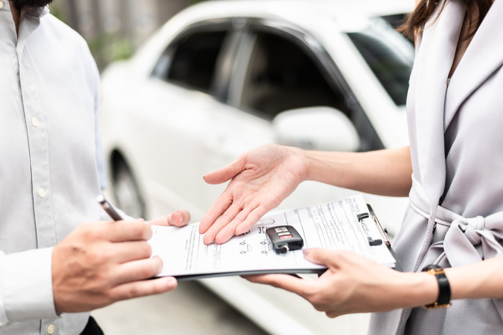 saleswoman holding clipboard with documents and car key on top waiting for man to sign documents