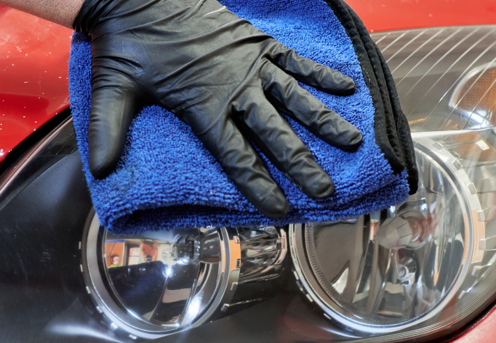 gloved hand of a mechanic wiping the headlights of a car with a cloth after having polished them and leaving them restored and shiny