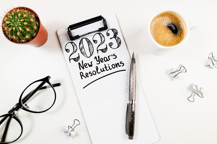 New year resolutions 2023 on desk. 2023 resolutions list with notebook, coffee cup on white table. Goals, resolutions, plan, action, checklist concept. New Year 2023 card top view